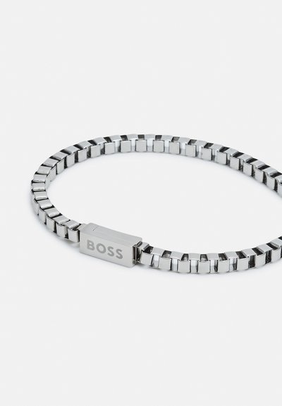 Bracelet en métal présentant des maillons rectangulaires au fini argent poli, avec un fermoir rectangulaire gravé de "BOSS".