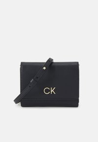 Bolso cruzado de cuero negro con un logo dorado "CK", diseño de solapa plegable, correa ajustable y textura suave.