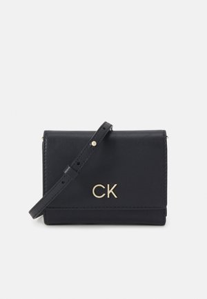Bolso cruzado de cuero negro con un logo dorado "CK", diseño de solapa plegable, correa ajustable y textura suave.