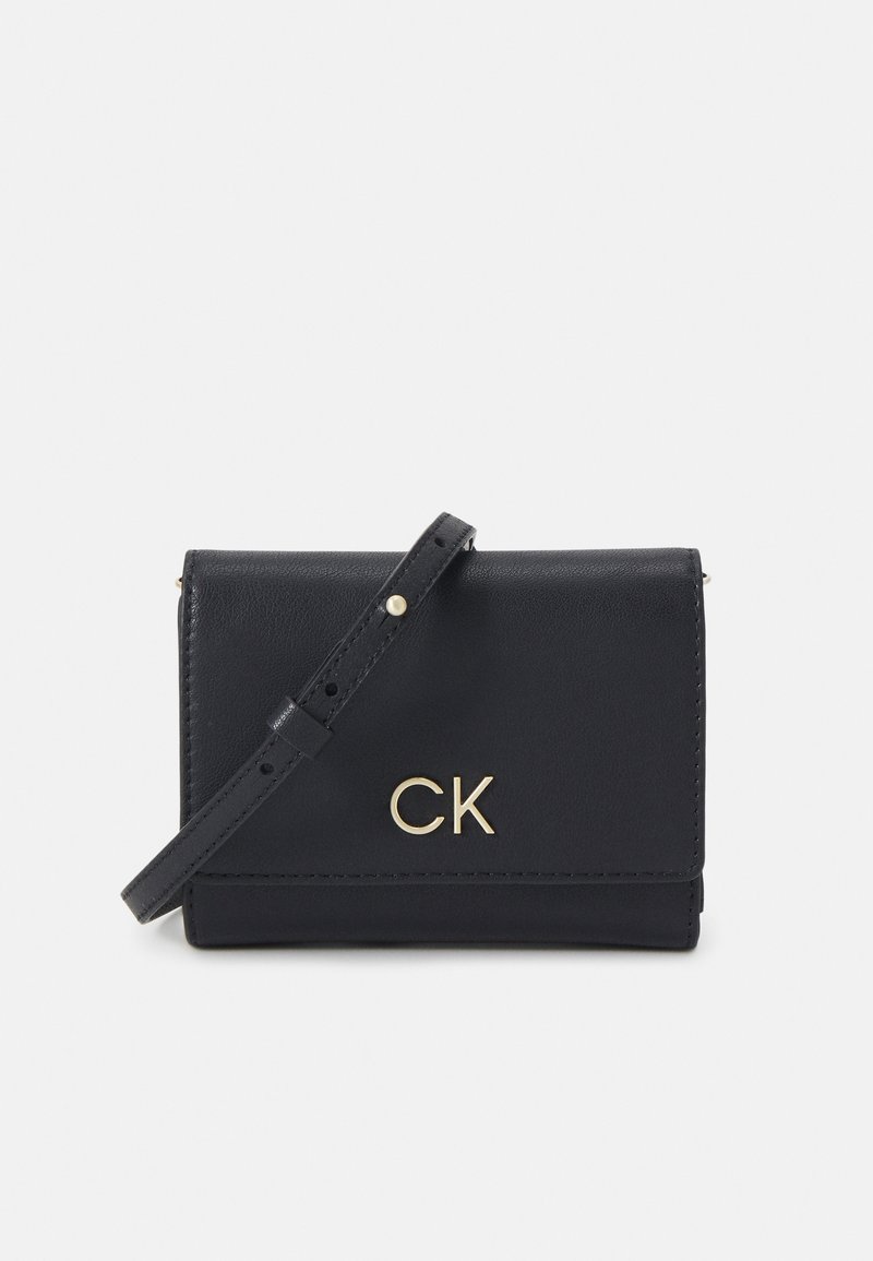 Bolso cruzado de cuero negro con un logo dorado "CK", diseño de solapa plegable, correa ajustable y textura suave.
