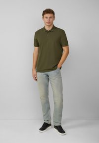 Oliwkowa koszulka polo z kołnierzykiem, w połączeniu z jasnoniebieskimi dżinsami i czarnymi trampkami, cechująca się prostym, klasycznym designem.
