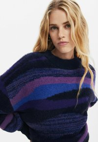 Overmaat gebreide trui in donkerblauw en paarse tinten, met een gestreept patroon met verschillende texturen en een ronde halslijn.