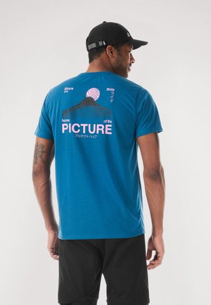 Maglietta di cotone blu con una grafica sul retro che mostra una montagna, un cerchio rosa e del testo. Maniche corte, vestibilità standard, texture liscia.