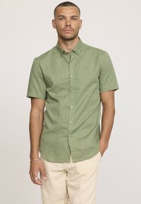 Chemise à manches courtes, couleur olive, avec des boutons, fabriquée en tissu léger. Elle présente un col boutonné et un logo brodé sur la poitrine.