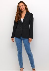 Černý blazer s klopami, dvěma knoflíky a předními kapsami. V páru se světle modrými skinny džíny a černými páskovými podpatky.