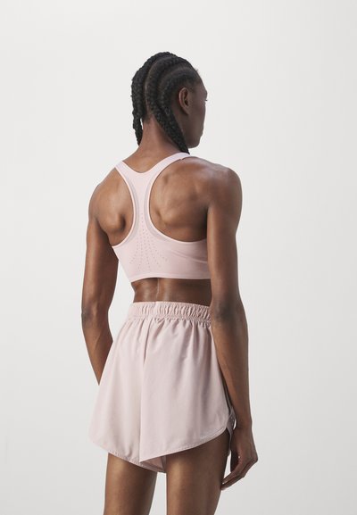 Sujetador deportivo rosa claro con un diseño de espalda nadadora, con detalles perforados. Combinado con shorts rosa claro a juego con una cinturilla elástica.