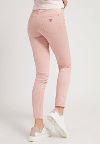 Różowe skinny jeans o gładkiej teksturze, z tylną kieszonką z trójkątnym logo, w połączeniu z białymi sneakersami.