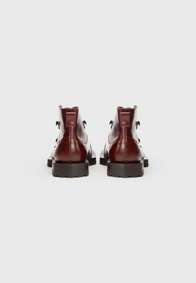 O pereche de botine elegante din piele roșie închisă, cu tălpi negre și rezistente, prezentate din spate pe un fundal alb.