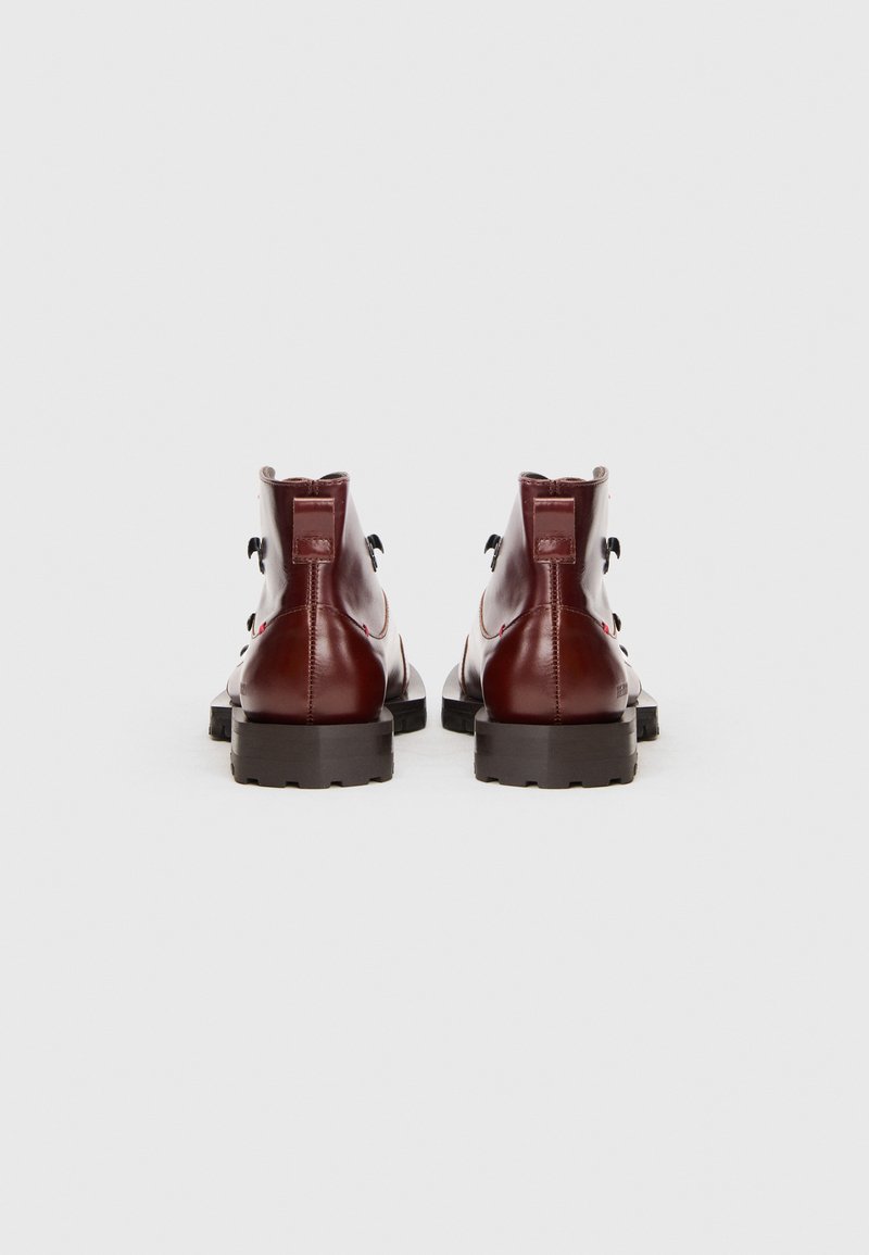 Ein Paar glänzende, dunkelrote Leder-Stiefeletten mit schwarzen, robusten Sohlen, von hinten auf einem weißen Hintergrund abgebildet.