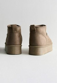 Bottines en daim marron avec un bout rond, une semelle plate et une languette à l'arrière. Finition texturée et motif de semelle en zigzag.