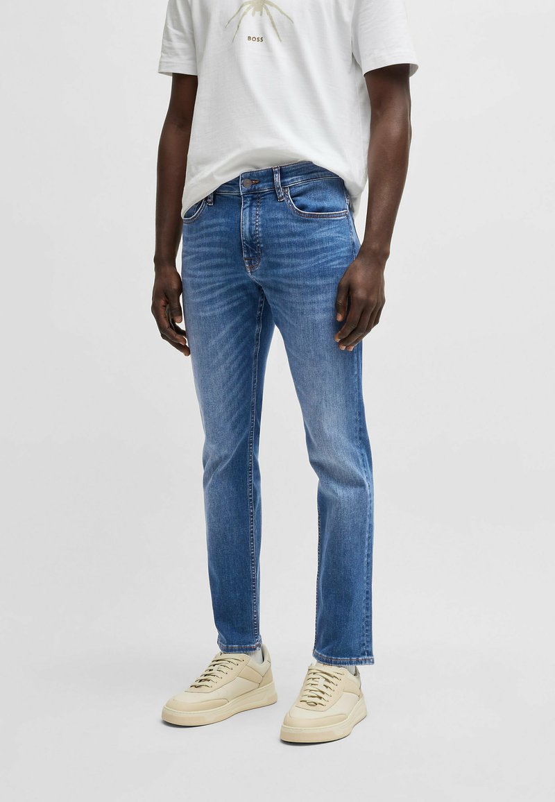 Vaqueros de mezclilla azul claro con corte slim, diseño de cinco bolsillos y un ligero desgaste. Combinados con una camiseta blanca y zapatillas beige.