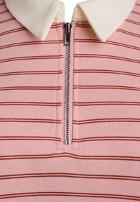 Top a righe bicolore, rosa e bianco, con chiusura con zip, dotato di colletto bianco e righe orizzontali rosse su un tessuto testurizzato.