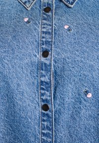 Denim shirt in light blue, featuring a button-down front with black buttons and pink embroidered cherry details. Distressed texture present.
