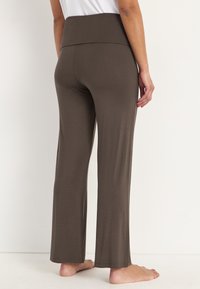 Braune, leichte, dehnbare Stoffhosen mit einem breiten, elastischen Bund. Die Beine sind leicht ausgestellt und der Saum ist ungesäumt.