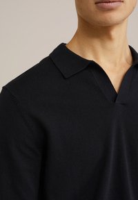 Svart stickad polo skjorta med V-hals och kort krage. Tyget verkar mjukt med en slät yta.