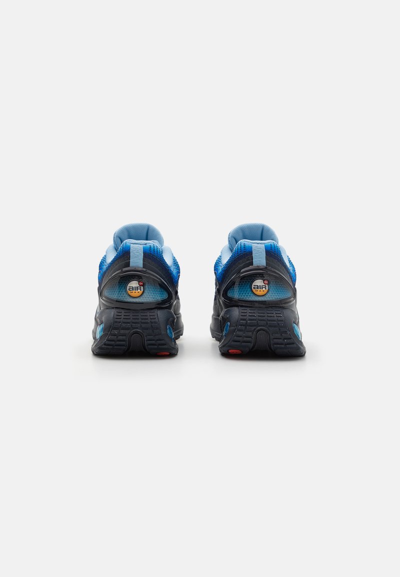 Baskets de sport noires et bleues avec une tige en mesh, un talon rond, un amorti Air visible et des accents de semelle extérieure bleu et rouge.