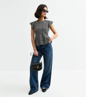 Top peplum floreale bianco e nero con maniche a cappuccio, abbinato a jeans a gamba larga a vita alta di colore blu e una piccola borsa nera.