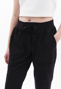 Zwarte broek met elastische tailleband en trekkoord. Gemaakt van een zachte, lichte stof, met zijzakken en een relaxed fit.