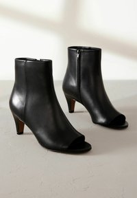 Stivali in pelle nera alla caviglia con punta aperta, un design elegante, tacco corto e cerniera laterale per la chiusura, caratterizzati da una texture liscia.