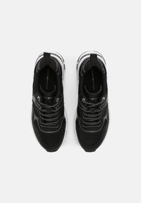 Baskets de sport noires avec une tige en mesh et synthétique, présentant des accents de rayures argentées, des lacets réfléchissants et une semelle blanche épaisse.