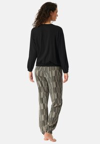 Zwarte langemouwen top met elastische zoom, gecombineerd met gestreepte tapered broeken in zwart en crèmewit. Zacht materiaal, comfortabele pasvorm, model op blote voeten.