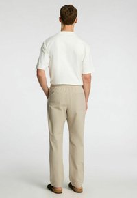 Krämfärgad t-shirt med korta ärmar, i kombination med beige byxor med elastisk midja som har en bakficka och en mjuk textur.