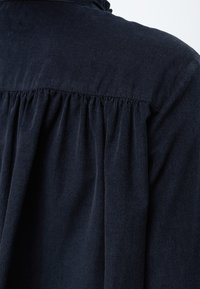 Κοντινό πλάνο ενός μπλε navy πουκαμίσου κοτλέ με λεπτομέρεια από σούρες στο ύφασμα κατά μήκος της πλάτης και στη ραφή των ώμων.