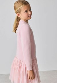 Svetloružové šaty s jemným pleteným vrchom a viacvrstvovou tylovou sukňou, s dlhými rukávmi a zaobleným výstrihom.