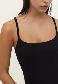 Débardeur noir à côtes avec des bretelles fines et ajustables et un décolleté carré. Le tissu a une texture lisse et un ajustement près du corps.