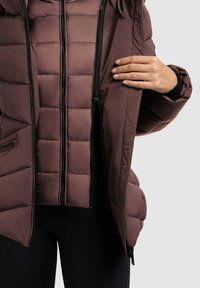 Brown puffer jacket with vertical quilted pattern, hood, and multiple black zippers. Currently unzipped to reveal interior details.