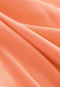 Baumwollstoff in einem sanften Korallton mit einer glatten Textur, sichtbaren Falten und Knicken, der ein leichtes und langlebiges Design aufweist.