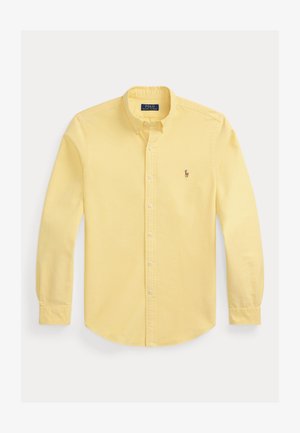 Camisa amarilla de botón con un cuello clásico, mangas largas y un pequeño logotipo bordado en el lado izquierdo del pecho. Textura de tela suave.