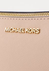 Pink textured fabric with a gold "MICHAEL KORS" logo. Includes a gold zipper detail along the top edge. Minimalistic design.