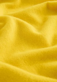 Gul stof med en blød tekstur, der viser fine strikkemønstre og bløde folder, hvilket skaber et glat, lysende udseende.