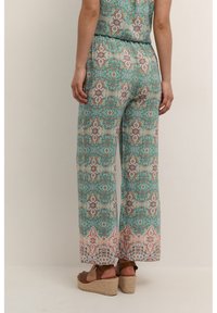 Wide-leg jumpsuit in a blue-green print featuring intricate floral patterns, with a loose fit and soft fabric. Worn with tan wedge sandals.