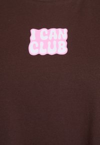 Brun t-shirt med en rosa, bubblig grafik som säger "JAG KAN KLUBBA". Kort ärm och mjukt, texturerat bomullstyg.