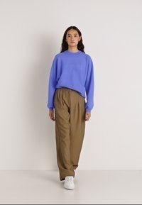 Ανοιχτό μωβ πουλόβερ με στρογγυλή λαιμόκοψη και ελαφρώς φαρδιά γραμμή, συνδυασμένο με καφέ παντελόνια ψηλόμεσα, φαρδιά πόδια και λευκά αθλητικά παπούτσια.