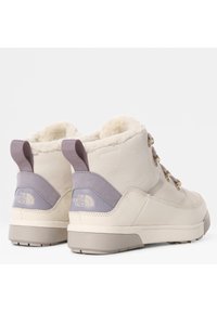 Botas de tobillo impermeables en color crema con un suave forro de piel sintética, detalles en gris y ojales de metal. Cuentan con una suela de goma texturizada y una tira de tiro.