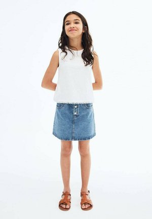 Haut sans manches blanc avec finition en dentelle, jupe en denim bleu avec des boutons à l'avant, et sandales à lanières marron. Fond blanc uni.