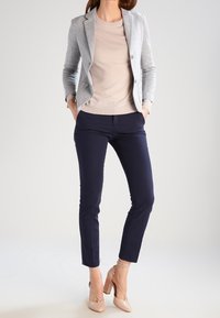 Grijze op maat gemaakte blazer, beige sweater, marineblauwe slim-fit broek en negehoge hakken. Gladde texturen en gestroomlijnde silhouet.