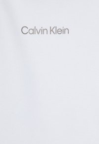 Tissu blanc avec une texture lisse, arborant le logo "Calvin Klein" en gris clair. Design simple et minimaliste.