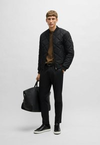 Black quilted bomber jacket, brown sweater, tailored black trousers, black sneakers with white soles, and a large black tote bag.