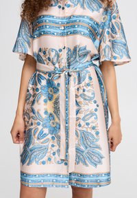 Rochie cu mânecă scurtă, până la genunchi, din satin roz pal, cu modele paisley și florale albastre, având talie legată și închidere cu nasturi.