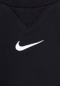Temno modra pulover s V-izrezom, rebrasto teksturo in belo Nikeovo puščico izšito na prsih.
