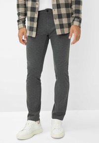 Pantaloni grigi a gamba affusolata realizzati in un tessuto morbido, con vita piatta, passanti per la cintura e tasche laterali, abbinati a sneaker bianche.
