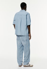 Vaaleansininen denimg shirt, jossa on rento istuvuus, lyhyet hihat ja hieman teksturoidut raidat, yhdistettynä löysästi istuviin vaaleansinisiin denimplälsi.