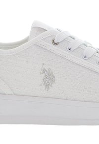 Bílé plátěné tenisky s texturovaným povrchem, s jemným stříbrným logem a bílými tkaničkami, na pevném bílém gumovém podpatku.