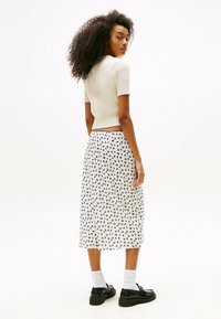 Top de punto blanco de manga corta combinado con una falda hasta la rodilla con un estampado abstracto en negro. El calzado son zapatos de plataforma negros.