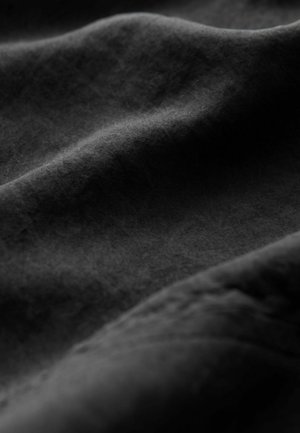 Tissu noir avec une surface douce et texturée affichant de douces vagues et de subtiles variations de teinte, créant un sentiment de profondeur et de mouvement.