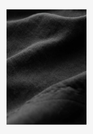 Tissu noir avec une surface douce et texturée affichant de douces vagues et de subtiles variations de teinte, créant un sentiment de profondeur et de mouvement.